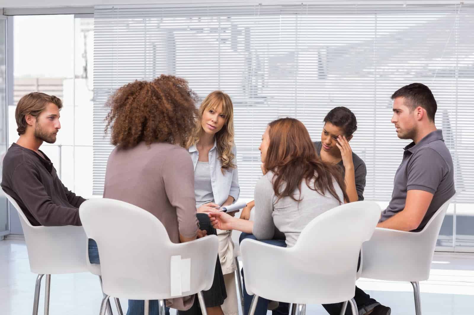 6 adults sitting on white chairs in a circle