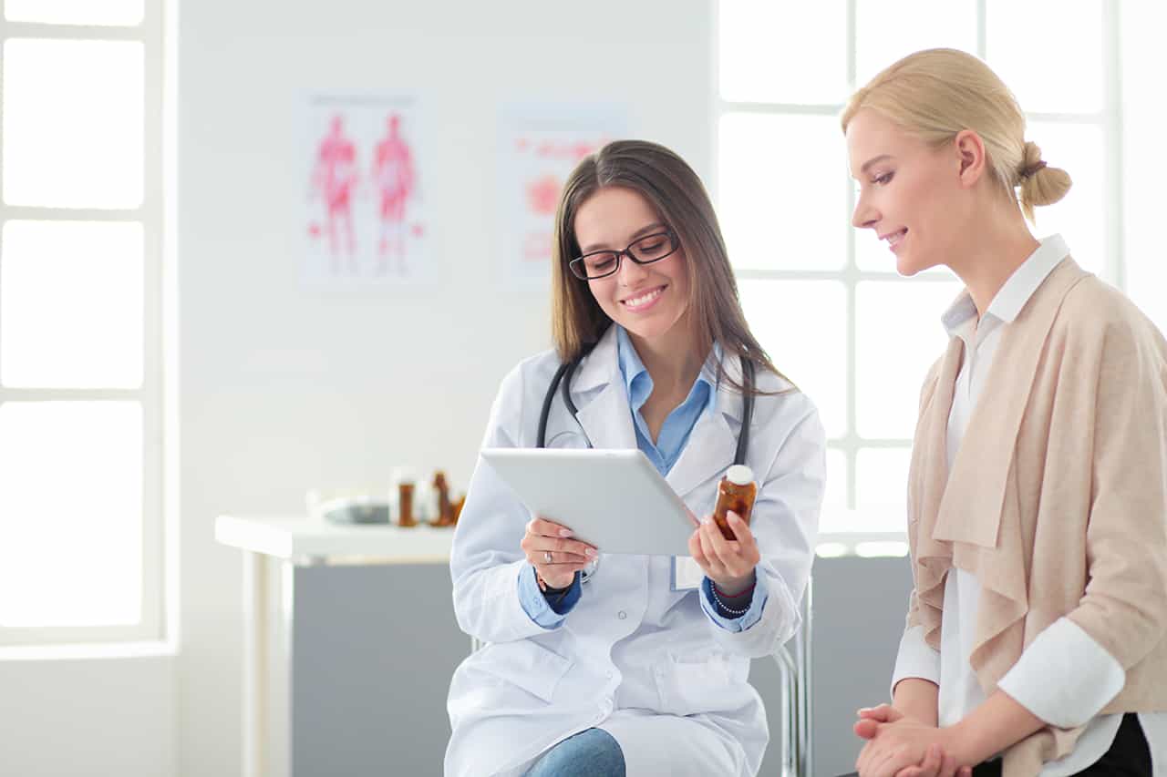 Nurse sitting with women standing looking at Ipad